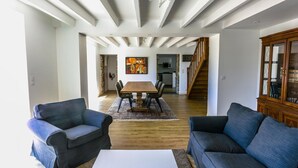 Amplia sala de estar con una mesa de comedor de madera, dos sofás y una escalera que conduce a un nivel superior.