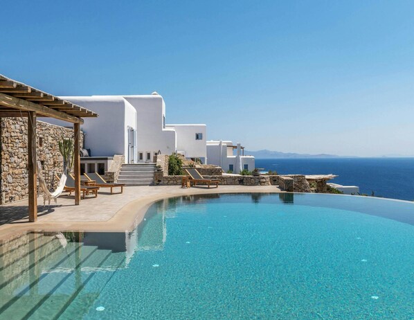 Ein Resort mit Infinity-Pool, weißen Gebäuden und Meerblick.