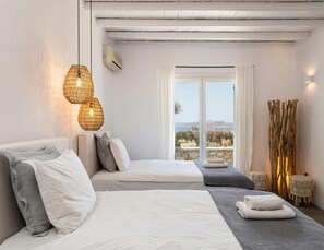 Ett sovrum med två sängar, ett stort fönster med utsikt, en takfläkt och en väggmonterad luftkonditioneringsanläggning.