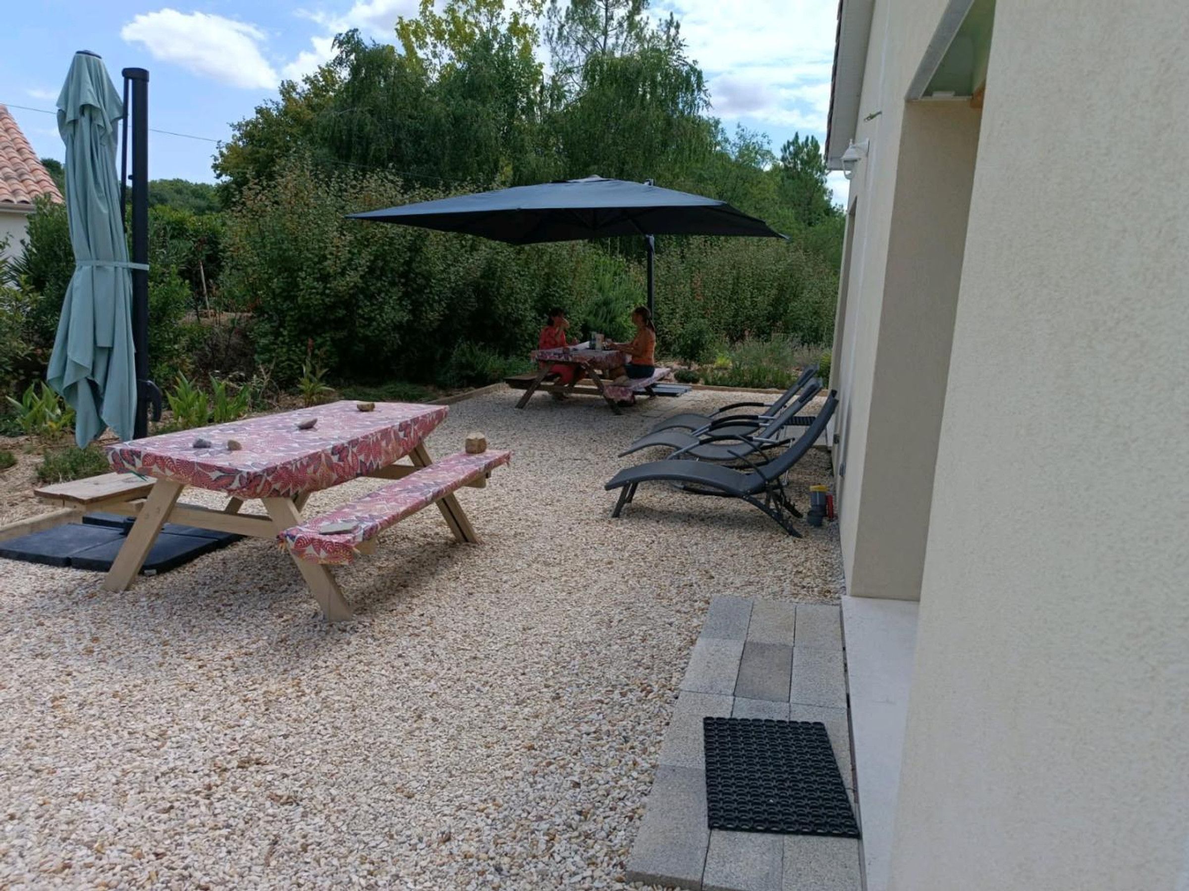 Un patio al aire libre con una mesa, bancos, una sombrilla y un espacio de descanso con sillones.