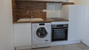 Cocina compacta con lavadora integrada, horno y lavabo con encimera de madera.