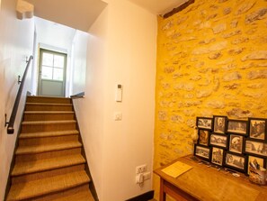 A staircase with carpeted steps leading to a door, a stone wall with framed pictures, and a wooden table with a yellow folder.
