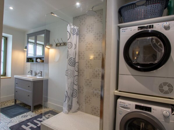 Ein kleines Badezimmer mit Waschmaschine, Dusche und Waschbecken.