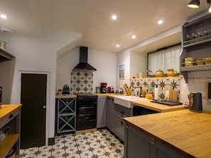 Cocina compacta con estufa negra, horno empotrado y microondas. Cuenta con encimera de madera y un lavamanos. El suelo presenta un diseño de baldosas con estampado de estrellas.