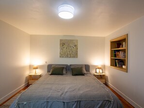 Ein Schlafzimmer mit einem großen Bett, zwei Nachttischen mit Lampen, einem Bücherregal und einer Deckenleuchte.
