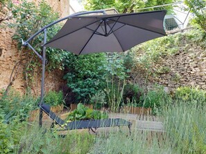 Ein Garten mit einer Terrasse, einem Liegestuhl und einem großen Sonnenschirm.