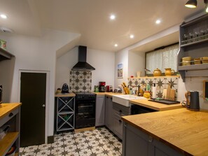 Cocina compacta con estufa negra, horno empotrado y microondas. Cuenta con encimera de madera y un lavamanos. El suelo presenta un diseño de baldosas con estampado de estrellas.
