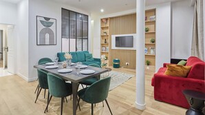 Un salon moderne comprenant un coin repas, un canapé rouge, un canapé turquoise et un téléviseur fixé au mur.