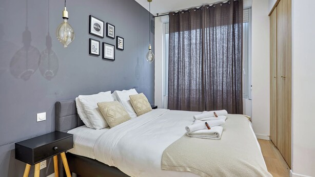Une chambre à coucher moderne avec un lit, des tables de chevet et une fenêtre avec des rideaux.