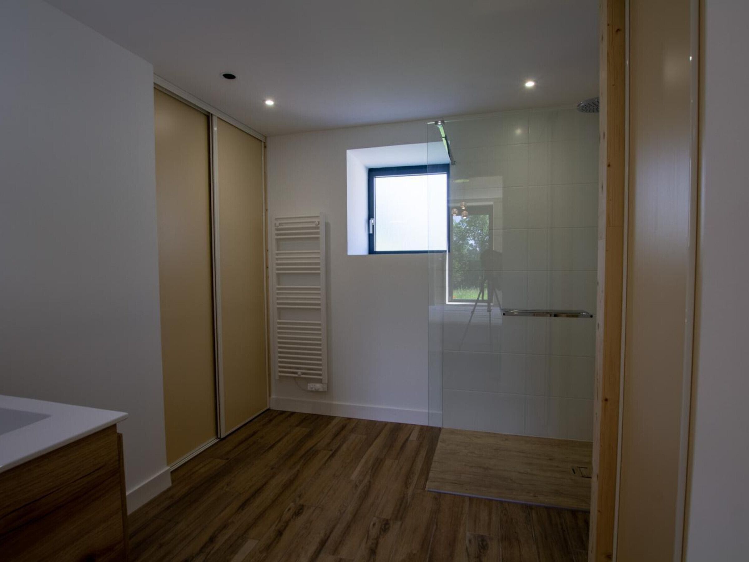 Une salle de bain moderne avec un plancher en bois, une douche en verre et une petite fenêtre qui laisse entrer la lumière naturelle.