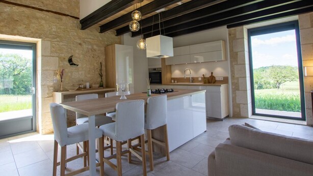 A modern kitchen with a central island, white cabinetry, and a stone wall. - Charming house with air conditioning, WiFi and pets allowed in Puycousin (Sorges et Ligueux en Périgord)