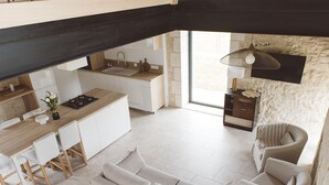 A modern kitchen with white cabinetry, a wooden countertop, and a built-in stove. There is a dining area with a white sofa and chairs, and a stone wall with a hanging light fixture. - Charming house with air conditioning, WiFi and pets allowed in Puycousin (Sorges et Ligueux en Périgord)