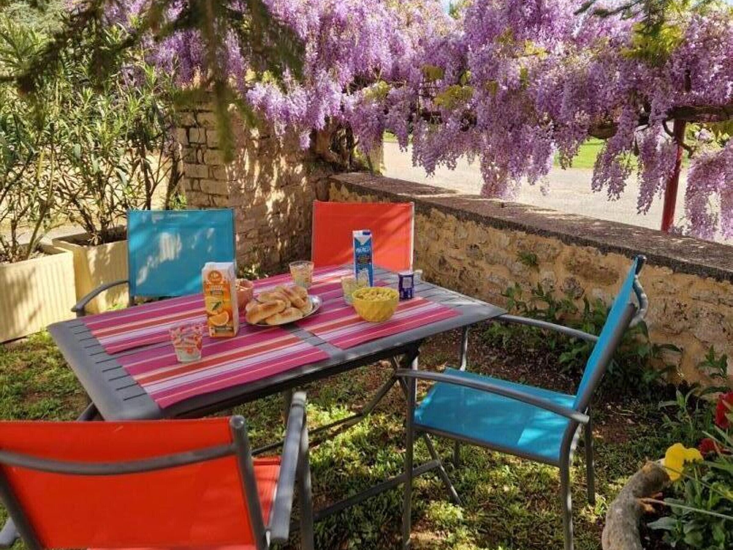 Un área de comedor al aire libre con una mesa dispuesta para dos, rodeada de sillas y vistas a árboles en floración de color púrpura.