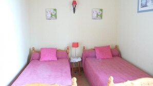 Une chambre avec deux lits en bois, chacun recouvert d’une couvre-lit rose et agrémenté d’oreillers assortis. Une petite table avec une lampe rouge se trouve entre les deux lits.