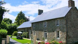 A stone building with a sloped roof, a small garden with red flowers, and a table and chairs outside. - Family house in Gouville-sur-Mer, near the English Channel, pets allowed (Gouville-sur-Mer)