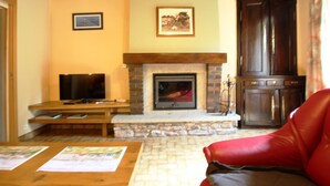 A living room with a fireplace, a television, a red leather sofa, and a wooden table with papers. - Family house in Gouville-sur-Mer, near the English Channel, pets allowed (Gouville-sur-Mer)