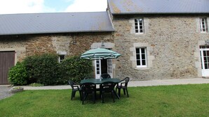 A stone building with a grey roof, a small garden with a table and chairs, and a green umbrella. - Family house in Gouville-sur-Mer, near the English Channel, pets allowed (Gouville-sur-Mer)