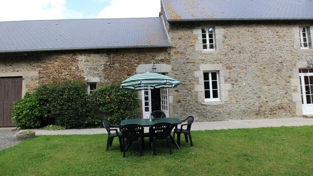 A stone building with a grey roof, a small garden with a table and chairs, and a green umbrella. - Family house in Gouville-sur-Mer, near the English Channel, pets allowed (Gouville-sur-Mer)