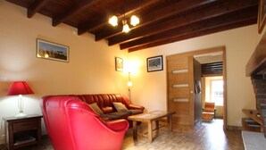 A cozy living room with a red leather sofa, a wooden table, and a lamp. There is a wooden door and a staircase visible in the background. - Family house in Gouville-sur-Mer, near the English Channel, pets allowed (Gouville-sur-Mer)