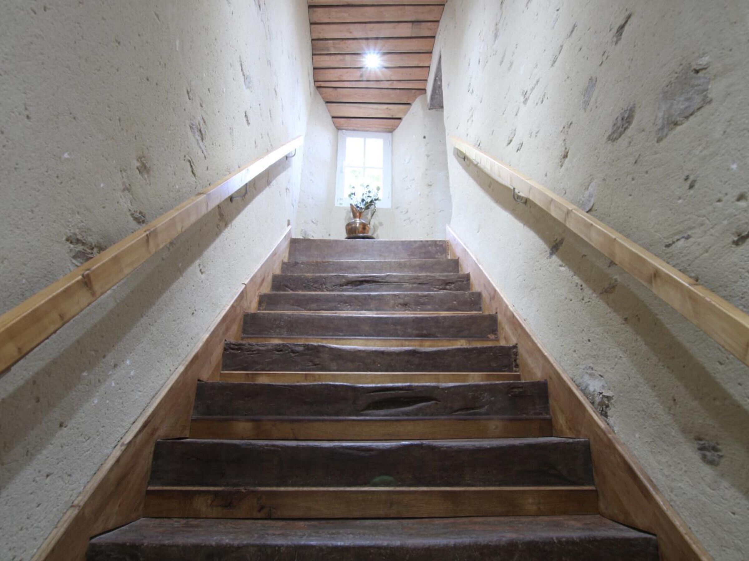 Una escalera de madera con barandilla de madera a ambos lados, que conduce a una ventana en la parte superior.