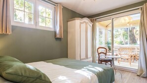 Ein Schlafzimmer mit einem Bett, einem Sessel und einem Tisch in der Nähe einer Glasschiebetür, die zu einem Außenbereich mit Sitzgelegenheiten und einem Tisch führt.