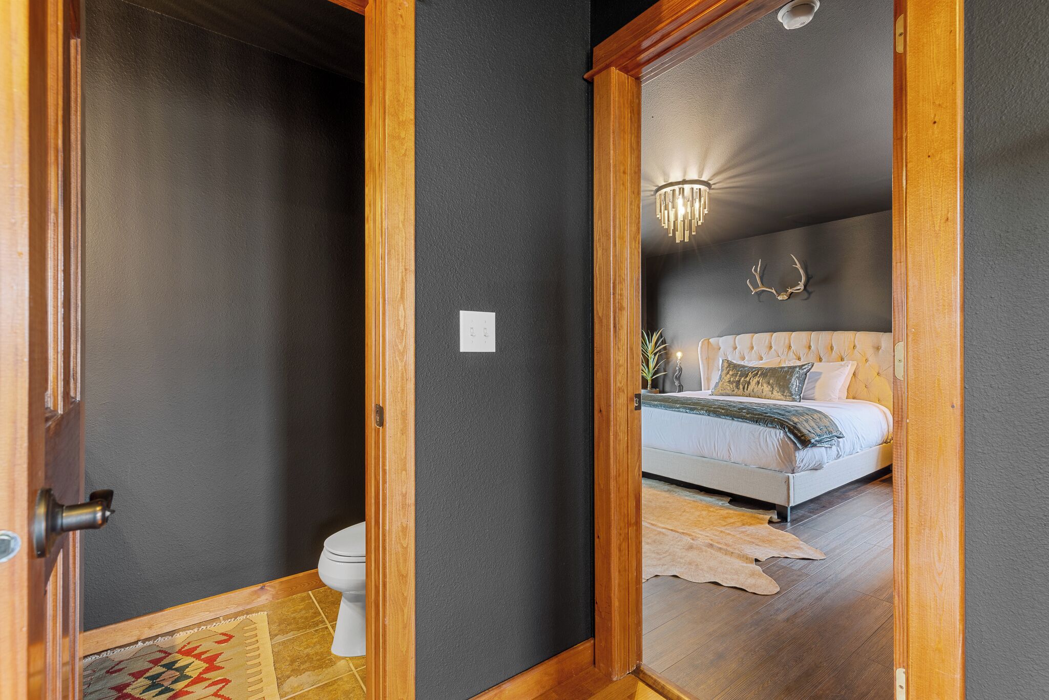 Un dormitorio con cama, candelabro y un adorno de cabeza de ciervo en la pared.