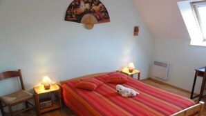 A bedroom with a wooden bed, two bedside lamps, a chair, and a wall-mounted fan. - Stone house near Utah Beach (Sainte-Marie-du-Mont)
