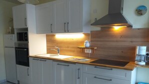 A modern kitchen with white cabinets, a stainless steel sink, a built-in oven, and a coffee maker. - Stone house near Utah Beach (Sainte-Marie-du-Mont)