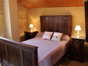 Un dormitorio con una cama de madera, dos mesitas de noche con lámparas y una pared de piedra.