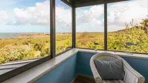 A room with a large window overlooking a coastal landscape, including a lighthouse and open fields. - Seaside House with Fireplace and Flowered Garden (La Hague)