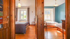 A room with two beds, wooden floors, and a view of the outdoors through windows. - Seaside House with Fireplace and Flowered Garden (La Hague)