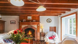A cozy room with a fireplace, wooden ceiling beams, a table with a red polka dot tablecloth, and two chairs. - Seaside House with Fireplace and Flowered Garden (La Hague)