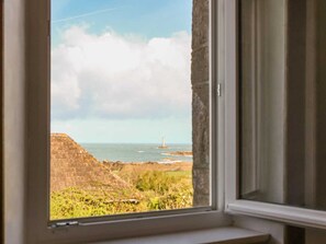 A window view of a coastal landscape with a lighthouse, stone walls, and greenery. - Seaside House with Fireplace and Flowered Garden (La Hague)