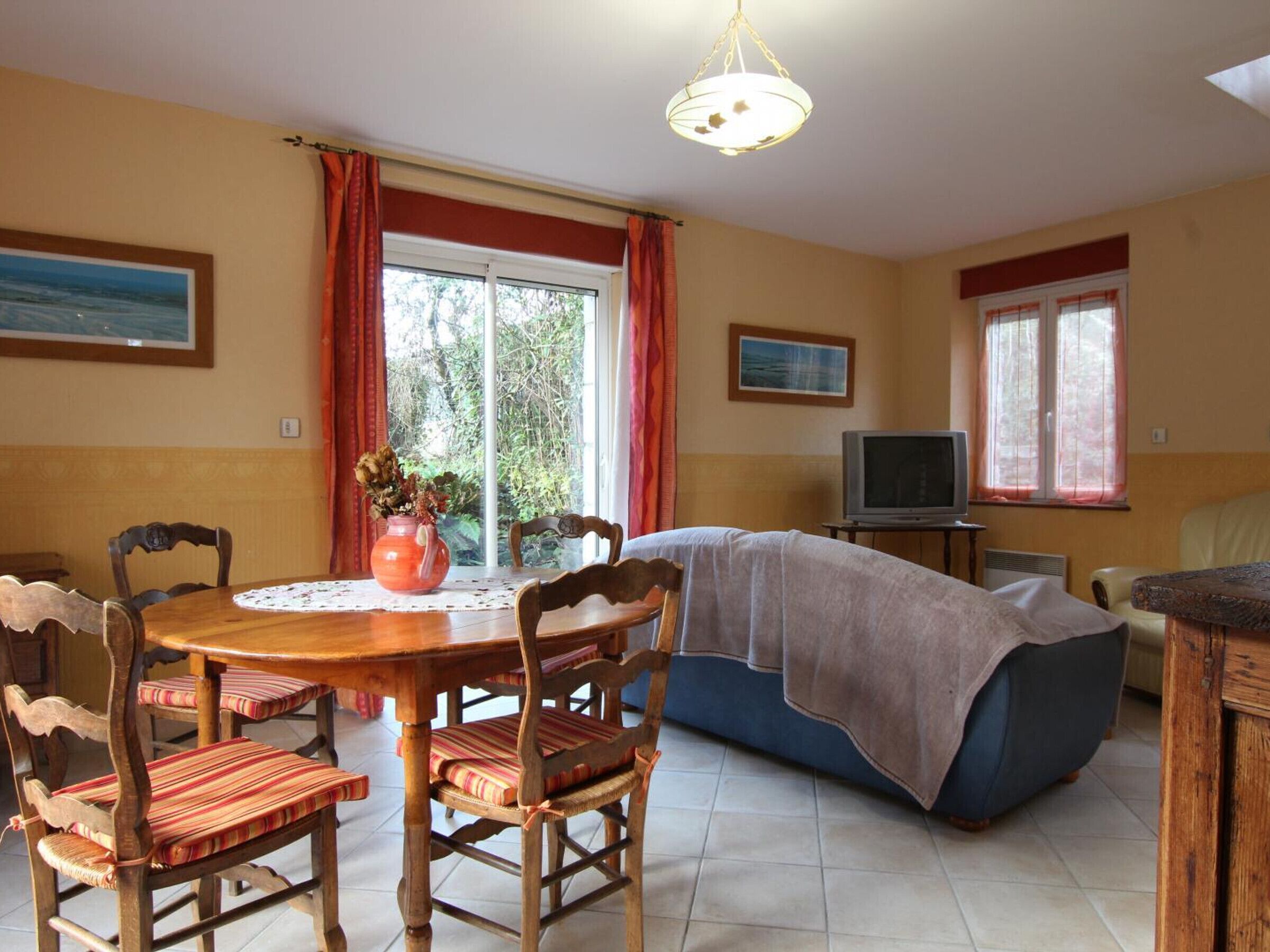 A cozy living room with a dining table, chairs, a sofa, a TV, and a large window with curtains.