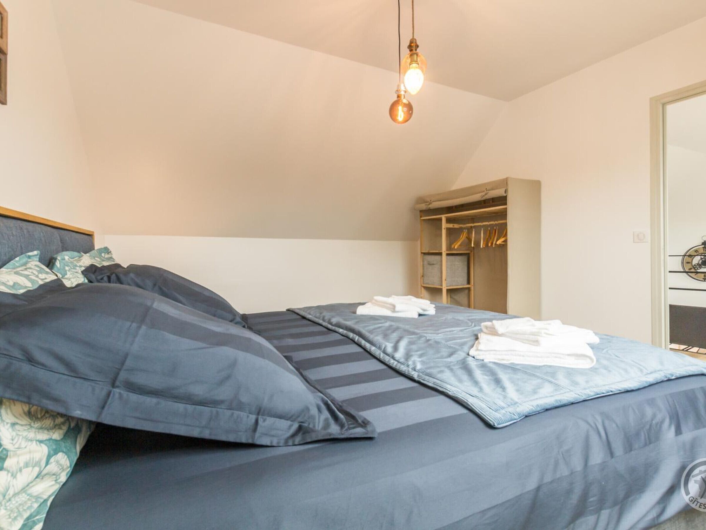 Une chambre à coucher comprenant un lit, des oreillers, une table de chevet, un luminaire suspendu et une armoire.