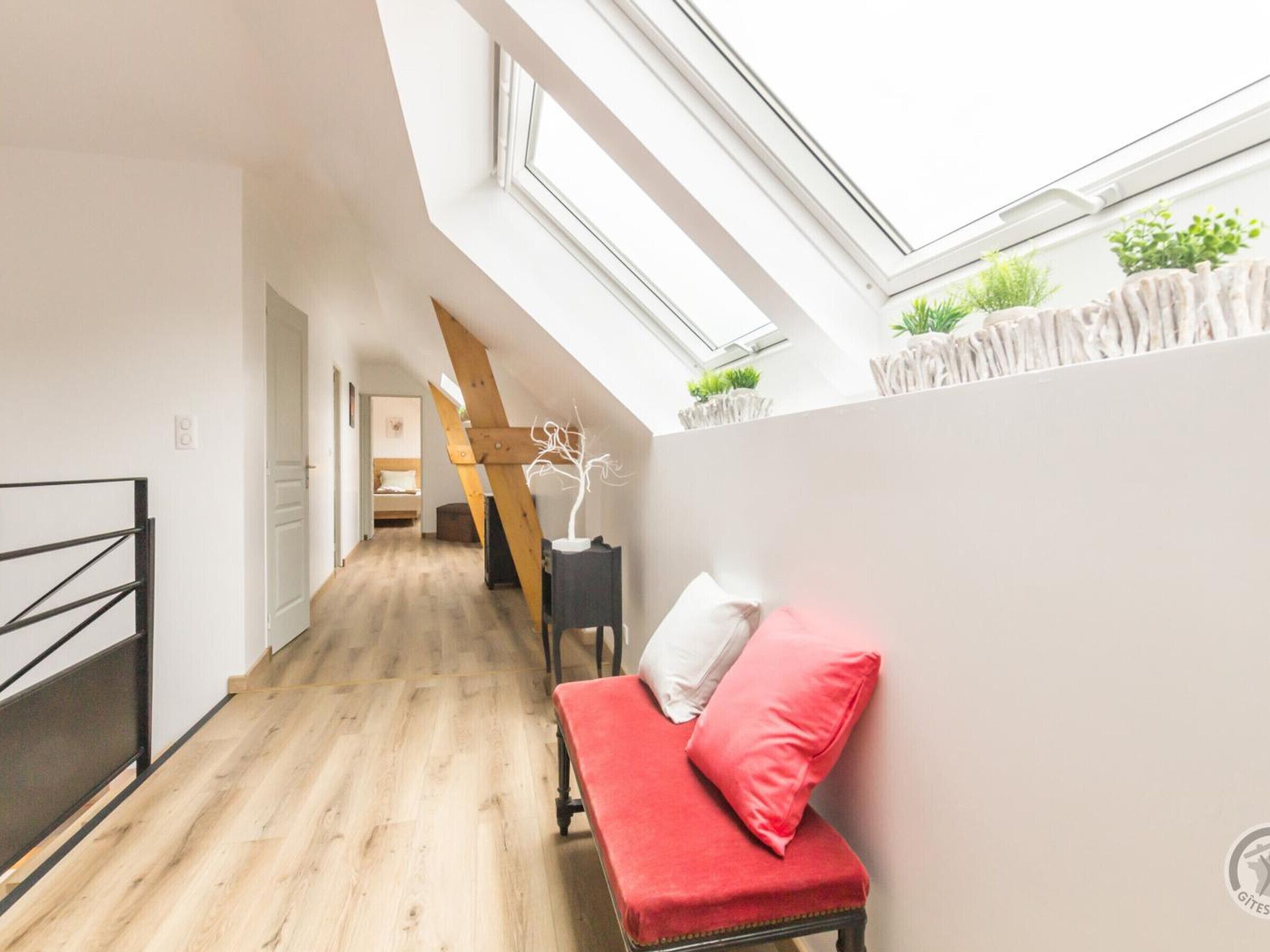A narrow hallway with wooden flooring, a red bench with white cushions, and a skylight above.