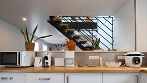 A modern kitchen with a microwave, coffee maker, toaster, and slow cooker on the counter. There is a staircase in the background. - Charming rental in La Hague with private garden, pets allowed (La Hague)