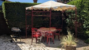 A covered outdoor seating area with a table and chairs, a grill, and a stone-tiled patio.