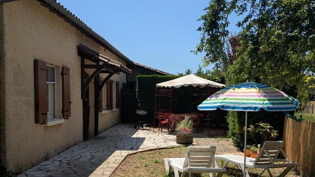 A patio with outdoor furniture, a striped umbrella, and a stone pathway leading to a building.