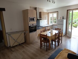 Eine Küche mit Holzausstattung, einer Mikrowelle, einem Backofen, einem Esstisch mit Stühlen und Blick ins Grüne.