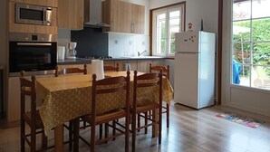 A kitchen with wooden cabinets, a microwave, stove, and a refrigerator. There is a dining table with chairs and a window with a view of greenery.