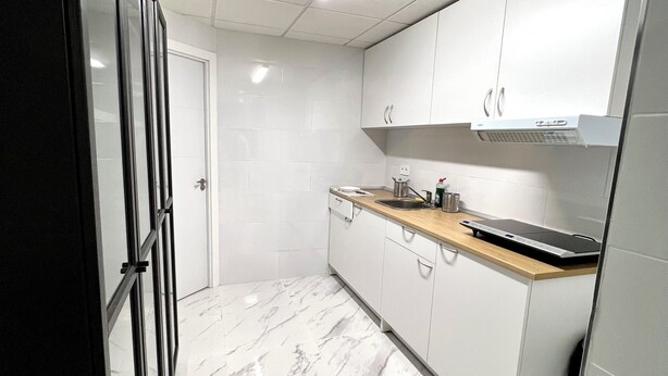 A modern kitchen with white cabinets, a marble floor, and a built-in oven. - Hostel Las Rosas (Madrid)