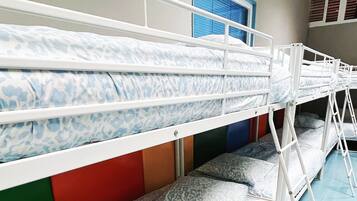Tweepersoonsbed met beddengoed met een patroon, een raam met zonwering en een deur met een blauwe omlijsting.