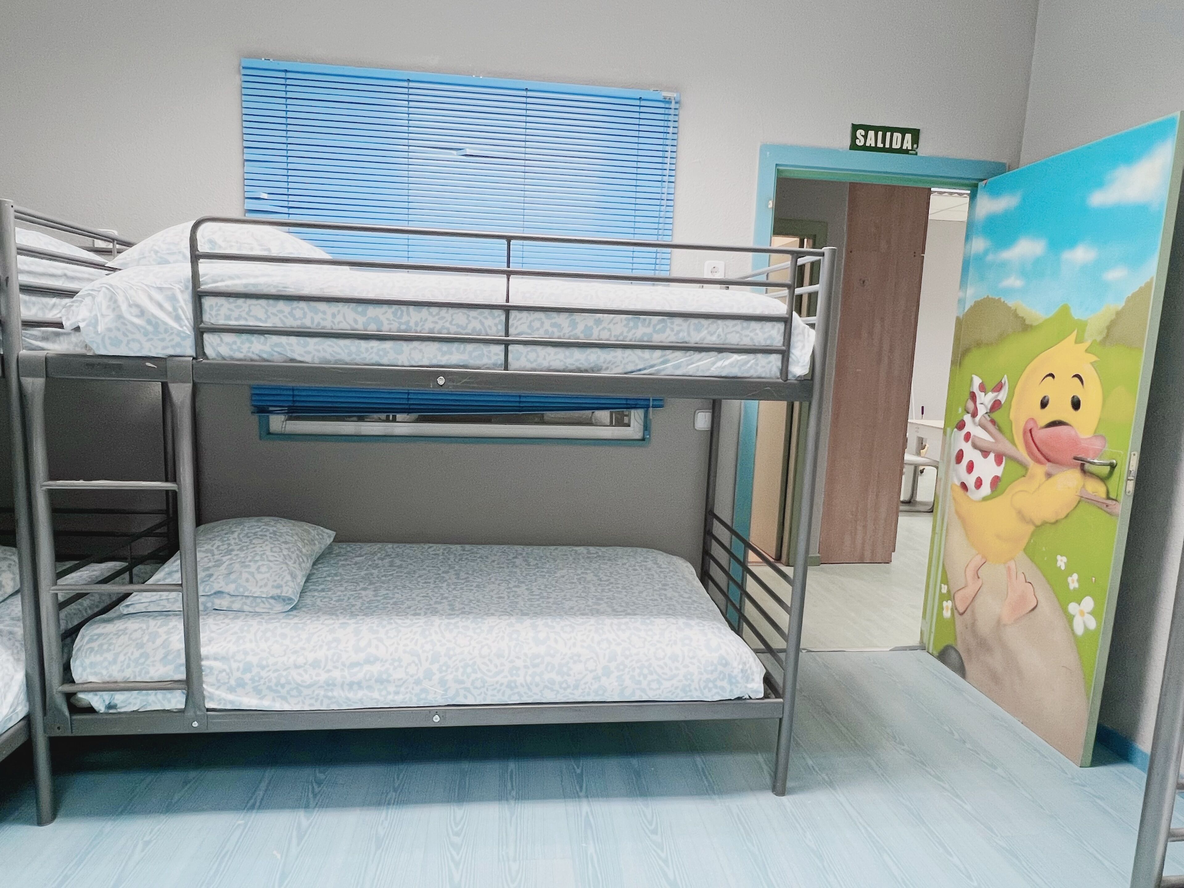 Habitación con literas, una ventana y una puerta con la etiqueta 'SALIDA'.