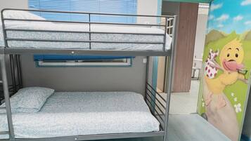 Uma cama beliche com roupa de cama estampada, uma janela com persianas azuis e uma porta com a etiqueta 'SALIDA'.