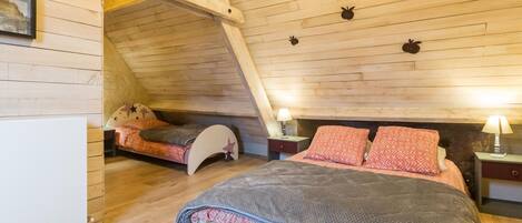 Une chambre mansardée chaleureuse, avec un plafond en pente, un lit superposé et un lit simple.