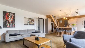 A modern living room with a grey sofa, a wooden coffee table, and a dining area with a staircase. - Semi-detached house with balcony in countryside, Wi-Fi, parking, pets allowed (Saint-Laurent-de-Terregatte)