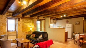 Un interior rústico con vigas de madera a la vista, una pared de piedra, un sofá, una mesa y una zona de kitchenette.