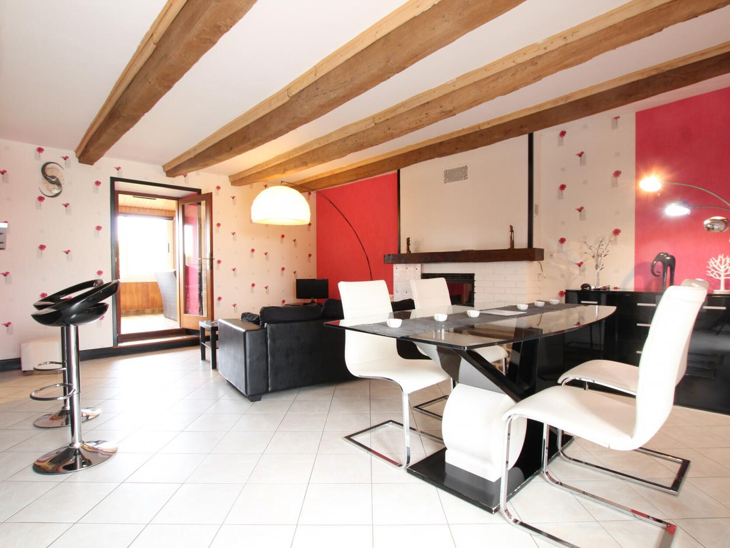 A modern dining area with a glass table, white chairs, and a red accent wall.