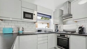 A modern kitchen with white cabinetry, a built-in microwave, a gas stove, and a window above the sink. - NEC Birmingham Airport Modern Village Retreat, Sleeps 7, Free Parking (Hampton in Arden)